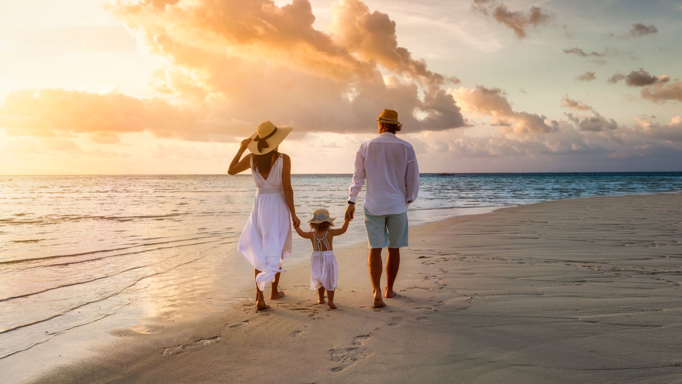 A elegant family in white summer clothing walks hand in hand down a tropical paradise beach during sunset tme and enjoys their vacation time